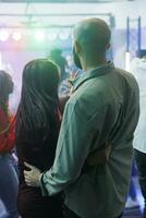 Jeune couple étreindre et permanent sur piste de dance tandis que faire la fête dans boîte de nuit. copain en portant petite amie taille tandis que aller en boîte ensemble, ayant amusement et profiter vie nocturne à discothèque photo