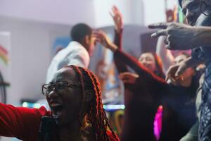 femme en chantant dans microphone bruyamment et en hurlant tandis que faire la fête avec copains dans boîte de nuit. insouciant africain américain clubber en criant tandis que ayant amusement et profiter karaoké dans club photo