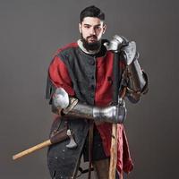 chevalier médiéval sur fond gris. portrait d'un guerrier brutal au visage sale avec une armure de cotte de mailles, des vêtements rouges et noirs et une hache de combat photo