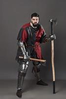chevalier médiéval sur fond gris. portrait d'un guerrier brutal au visage sale avec une armure de cotte de mailles, des vêtements rouges et noirs et une hache de combat photo