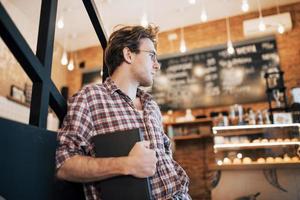 Jeune homme talentueux en chemise décontractée dessin croquis dans un ordinateur portable profitant du temps libre dans un café. Étudiant qualifié écrivant ses devoirs dans le bloc-notes assis dans le coworking photo