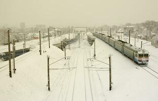 un long train de voitures voyageurs se déplace le long de la voie ferrée. paysage ferroviaire en hiver après les chutes de neige photo