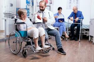 médical des trucs en présentant une brochure avec arythmies à handicapé Sénior femme séance dans fauteuil roulant. homme avec handicapées ,marche Cadre séance dans hôpital lit. santé se soucier système, clinique les patients. photo