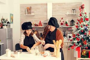 content fille sur Noël journée portant tablier fabrication biscuits ensemble avec grand-mère. de bonne humeur joyeux adolescent fille portion Sénior femme en train de préparer sucré biscuits à célébrer hiver vacances. photo