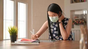 une fille portant un masque assise au travail. elle travaille à la maison pour se protéger contre le virus covid-19.