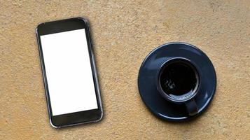 gros plan sur un smartphone à écran vierge et une tasse à café sur un sol en béton jaune, vue de dessus. photo
