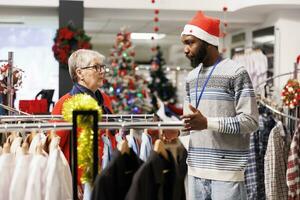 ouvrier portion personnes âgées femme à choisir droite en forme de formel tenue, en train de préparer à assister de fête dîner sur Noël vacances. africain américain boutique employé recommander vêtements pour client. photo