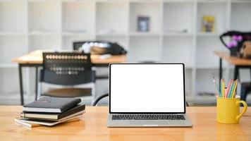 photo recadrée d'un ordinateur portable avec des cahiers et des articles fixes sur un bureau en bois dans un bureau moderne.