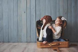 enfant heureux en chapeau de pilote et petite fille jouant avec une vieille valise. enfance. fantaisie, imaginaire. concept de voyage photo