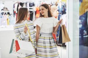 belle journée pour faire du shopping. deux belles femmes avec des sacs à provisions se regardant avec le sourire en marchant dans le magasin de vêtements photo