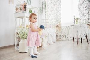 notion d'enfance. petite fille en robe mignonne joue avec du fil coloré. chambre d'enfant vintage blanche photo