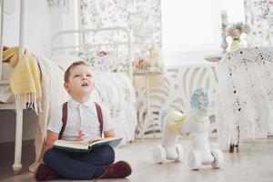 mignon petit garçon va à l'école pour la première fois. enfant avec cartable et livre. enfant fait une mallette, chambre d'enfant sur un fond. retour à l'école photo