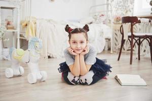 mignonne petite fille enfant lisant un livre dans la chambre. enfant avec couronne assis sur le lit près de la fenêtre photo