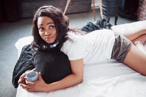 heureuse belle fille africaine en vêtements de nuit s'étirant souriant assis sur le lit à la maison s'est réveillé le matin par une journée ensoleillée photo