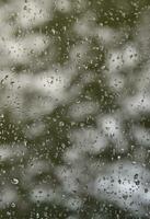 une photo de gouttes de pluie sur la vitre avec une vue floue des arbres verts en fleurs. image abstraite montrant des conditions météorologiques nuageuses et pluvieuses