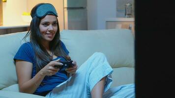 femme séance sur canapé en jouant vidéo Jeux, souriant relaxant profiter le soir. excité déterminé joueur en utilisant manette joysticks clavier playstation jeu et ayant amusement gagnant électronique Jeu photo