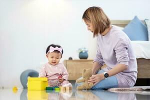 asiatique mère est en jouant avec sa jolie souriant bébé fille avec en bois jouet bloquer tandis que dépenses qualité temps dans le lit pour famille bonheur et parentalité photo