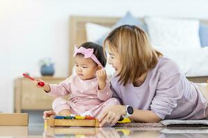 asiatique mère est en jouant avec sa jolie souriant bébé fille avec en bois jouet bloquer tandis que dépenses qualité temps dans le lit pour famille bonheur et parentalité photo