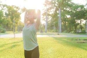 femelle joggeur. en forme Jeune asiatique femme avec vert tenue de sport élongation muscle dans parc avant fonctionnement et profiter une en bonne santé Extérieur. aptitude coureur fille dans Publique parc. bien-être étant concept photo