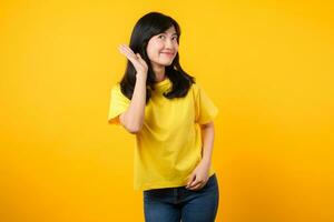 Capturer attention portrait de Jeune asiatique femme. portant une Jaune T-shirt et denim jeans, penche dans à surprendre et écouter, évoquant curiosité et intrigue. accrocheur promotions et remises. photo