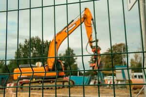 Orange excavatrice à construction site vu par clôture grille photo