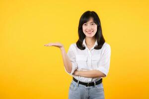 content Jeune asiatique femme portant blanc chemise et denim jean les plantes en présentant ou montrant ouvert main paume avec copie espace pour produit isolé sur Jaune Contexte. présent produit La publicité concept. photo