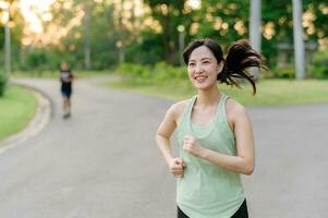 en forme asiatique Jeune femme le jogging dans parc souriant content fonctionnement et profiter une en bonne santé Extérieur mode de vie. femelle joggeur. aptitude coureur fille dans Publique parc. en bonne santé mode de vie et bien-être étant concept photo