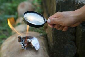 proche en haut main tenir grossissant verre à faire Feu pour brûlant papier. concept, science expérience à propos convexe lentille, tenir grossissant verre entre le Soleil et Tinder. pratique survie compétence photo