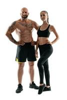 athlétique homme dans noir short et baskets avec brunette femme dans leggings et Haut posant isolé sur blanc Contexte. aptitude couple, Gym concept. photo