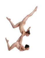 deux souple les filles gymnastes dans beige justaucorps sont performant des exercices à l'envers vers le bas en utilisant soutien et posant isolé sur blanc Contexte. fermer. photo