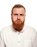 portrait de une jeune, joufflu, rousse homme dans une blanc chemise fabrication visages à le caméra, isolé sur une blanc Contexte photo