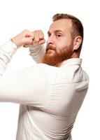 portrait de une jeune, joufflu, rousse homme dans une blanc chemise fabrication visages à le caméra, isolé sur une blanc Contexte photo