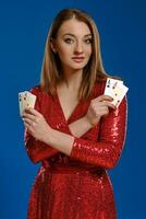 blond femme avec se maquiller, dans rouge paillette robe est montrant quatre as, posant sur bleu Contexte. jeu, poker, casino. fermer. photo