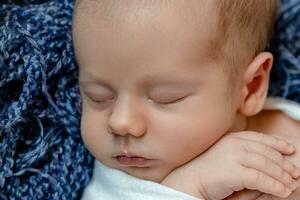 nouveau née - bébé, visage fermer. le en train de dormir nouveau née garçon en dessous de une blanc tricoté couverture mensonges sur le bleu fourrure. photo