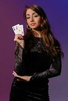 brunette femme dans noir velours robe montrant deux en jouant cartes, posant contre coloful Contexte. jeux d'argent divertissement, poker, casino. fermer. photo