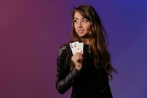 brunette femme dans noir velours robe montrant deux en jouant cartes, posant contre coloful Contexte. jeux d'argent divertissement, poker, casino. fermer. photo