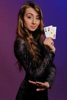 brunette fille dans noir velours robe montrant deux en jouant cartes, posant de côté sur coloful Contexte. jeux d'argent divertissement, poker, casino. fermer. photo