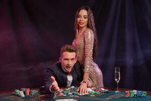 homme en jouant poker à casino séance à table avec piles de puces, argent, Champagne, cartes. célébrer gagner avec femme. noir Contexte. fermer. photo