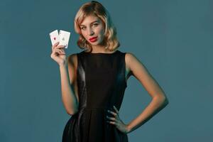 blond fille dans noir élégant robe montrant deux en jouant cartes, posant contre bleu Contexte. jeux d'argent divertissement, poker, casino. fermer. photo