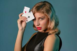 blond fille dans noir élégant robe montrant deux en jouant cartes, posant contre bleu Contexte. jeux d'argent divertissement, poker, casino. fermer. photo