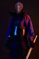 proche en haut tir, kendo combattant portant dans un armure, traditionnel kimono, casque pratiquant martial art avec shinaï bambou épée, noir Contexte. photo