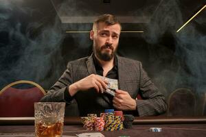 Beau barbu homme est en jouant poker séance à le table dans casino. photo