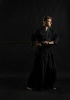 kendo gourou portant dans une traditionnel Japonais kimono est pratiquant martial art avec le shinaï bambou épée contre une noir studio Contexte. photo