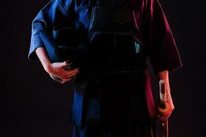 kendo combattant portant dans un armure, traditionnel kimono est en portant le sien casque et shinaï bambou épée tandis que posant sur une noir Contexte. proche en haut. photo