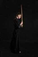 kendo gourou portant dans une traditionnel Japonais kimono est pratiquant martial art avec le shinaï bambou épée contre une noir studio Contexte. photo