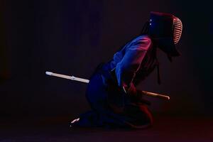 proche en haut tir, kendo combattant portant dans un armure, traditionnel kimono, casque pratiquant martial art avec shinaï bambou épée, noir Contexte. photo