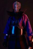 proche en haut tir, kendo combattant portant dans un armure, traditionnel kimono, casque pratiquant martial art avec shinaï bambou épée, noir Contexte. photo