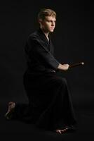 kendo gourou portant dans une traditionnel Japonais kimono est pratiquant martial art avec le shinaï bambou épée contre une noir studio Contexte. photo