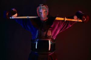 proche en haut tir, kendo combattant portant dans un armure, traditionnel kimono, casque pratiquant martial art avec shinaï bambou épée, noir Contexte. photo