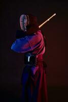 proche en haut tir, kendo combattant portant dans un armure, traditionnel kimono, casque pratiquant martial art avec shinaï bambou épée, noir Contexte. photo